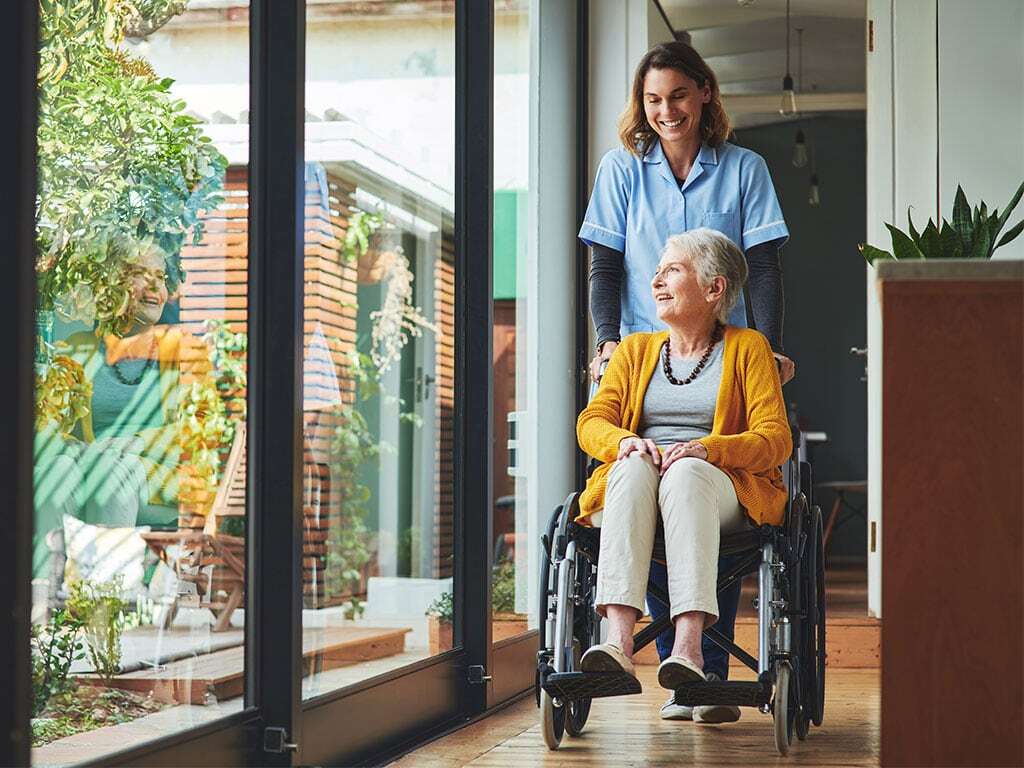 Pflegerin mit Patientin im Rollstuhl; © iStock 1315315044